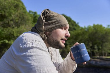 Genç adam sabahları dışarıda oturup kahve ve sıcak bir şeyler içmeyi seviyor. Onun ifadesi rahatlama ve refahın bir parçasıdır ve doğada kamp yapmanın sükunetini yansıtır..