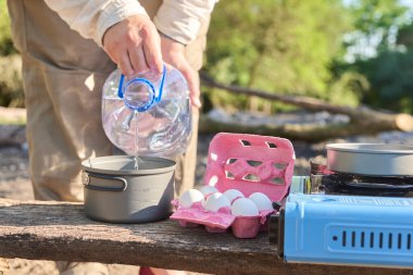 Kamp yaparken yemek pişirme sürecinin bir parçası olarak, tanınmayan kişi bir tencereye içme suyu döküyor..