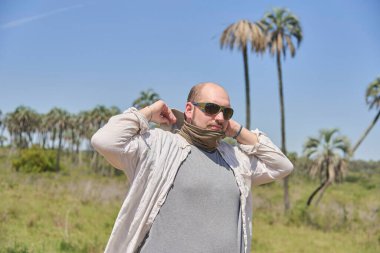 Uzun kollu gömlek ve güneş gözlüğü takan bir adam güneşli bir ortamda kendini güneşten korumak için şapka takıyor. Konsept: sağlık sorunlarını önlemek için seyahat ederken özbakım ve cilt bakımı