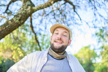 Doğada mutluluk ve refahın bir ifadesi ile gülümseyen genç bir adamın portresi; arka plan, fotokopi alanı ile, parlak gökyüzü ve odak dışı ağaçlar.