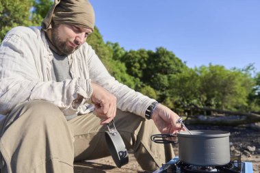 İspanyol bir adam, portatif kamp sobası kullanarak tencerede ısıttığı suyun sıcaklığını ölçüyor..