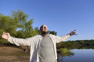 Kolları açık ve mutlu bir yüz ifadesi olan bir adamın portresi, bir derenin kıyısında. El Palmar Ulusal Parkı, Entre Rios, Arjantin