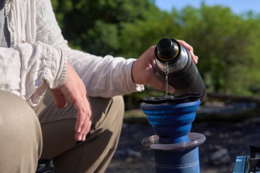 Açık hava kahve yapma süreci: tanınmayan bir gezgin kahvaltısını hazırlamak için içinde taze öğütülmüş kahve bulunan katlanmış seyahat filtresine sıcak su döker.