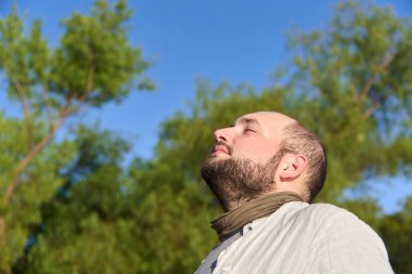 Huzur ve sükunet ifadesiyle gülümseyen genç bir adamın samimi portresi. Sabah güneşinin yumuşak ışığıyla aydınlanıyor. Sahne, refahı, sakinliği ve olumlu duyguları iletir. Düşük açı görünümü.