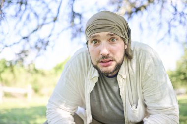 Kameraya bakan, korkmuş bir ifadeyle bakan kendini ifade eden genç bir adamın portresi, güneşli bir günde açık havada..