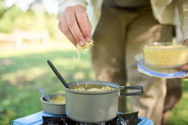 Tanınmayan biri, taşınabilir gaz sobasıyla taze pişmiş bir tencere pirincin üzerine rendelenmiş peynir yayıyor. Seçici odaklı kompozisyon ve kopyalama alanı.