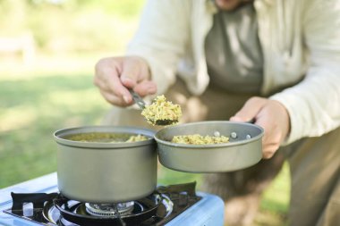 Tanınmayan erkek gezgin portatif gaz sobasında pişirdiği sebzelerle pirinç servis ediyor. Seçici odaklı kompozisyon ve kopyalama alanı.
