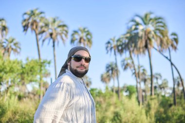 Güneşli bir günde arka planda palmiye ağaçları olan güneş gözlüklü genç bir adamın portresi. El Palmar Ulusal Parkı 'nda, Entre Rios, Arjantin' de doğanın tadını çıkaran bir gezgin..