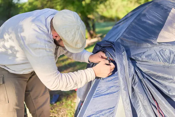 Erkek gezgin, gün batımında çadırını açık havada kurarken yağmurlu havayı bağlıyor..