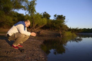 Gezgin, güneşin ilk ışıklarıyla aydınlatılan sakin doğal bir manzarada gün doğumunda bir derenin kıyısında ellerini ve yüzünü yıkıyor. El Palmar Ulusal Parkı, Entre Rios, Arjantin.
