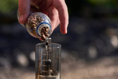 Kahve öğütme işlemi: Güneşli bir sabahta, açık havada, öğütücüye kızarmış fasulye döken bir elin yakın görüntüsü.