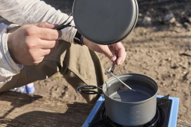 Tanınmayan bir adam, portatif kamp sobası kullanarak tencerede ısıttığı suyun sıcaklığını ölçüyor..