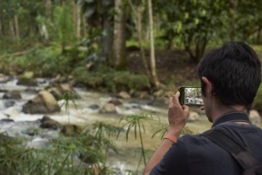 Genç adam cep telefonuyla doğal bir yerde fotoğraf çekiyor, Fonce nehri, El Gallineral Parkı, San Gil, Santander, Kolombiya.