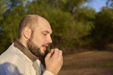 Şafak vakti bir derenin kıyısında oturan İspanyol erkek gezgin kurabiye yemekten zevk alırken gün ışığının ilk ışıklarını alıyor. El Palmar Ulusal Parkı, Entre Rios, Arjantin.
