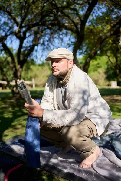 Genç adam çadır direklerini elinde tutuyor ve onu barışçıl bir kamp alanına kurma sürecini başlatıyor. Çevre yeşil ve hava güneşli..