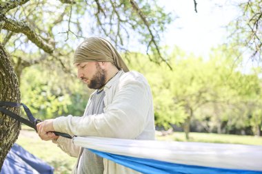 Doğada, ağaçların gölgesinde dinlenmek için hamak asan genç bir İspanyol. Kavram: açık havada eğlenmek.