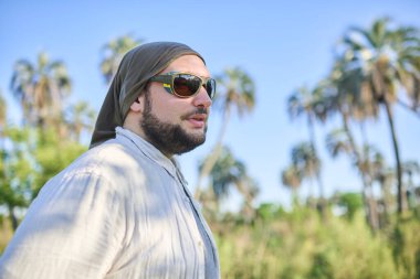 Güneşli bir günde arka planda palmiye ağaçları olan güneş gözlüklü genç bir adamın portresi. El Palmar Ulusal Parkı 'nda, Entre Rios, Arjantin' de doğanın tadını çıkaran bir gezgin..