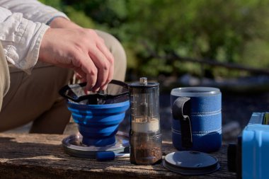Tanımlanamayan erkek gezgin kahvaltısını hazırlıyor, açık havada taze kahve hazırlıyor, manuel seyahat öğütücüsü ve katlama filtresi kullanıyor..