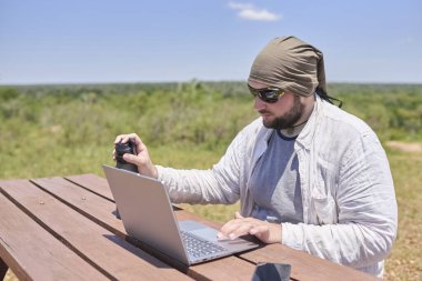 Güneşli bir günde dışarıda bir masada dizüstü bilgisayarıyla çalışan genç bir İspanyol. Dijital göçebe, özgürlüğün tadını çıkarırken uzaktan çalışıyor..