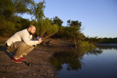 Gezgin şafak vakti, güneşin ilk ışıklarıyla aydınlatılan sakin doğal bir manzarada ellerini ve yüzünü bir derenin kıyısında yıkıyor. El Palmar Ulusal Parkı, Entre Rios, Arjantin.