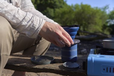 Açık havada kahve yapma işlemi, tanınmayan bir gezgin içeceği süzmek için katlanan seyahat filtresini fincanın üzerine koyar..