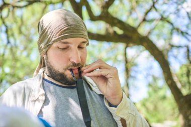 Genç İspanyol adam ağzıyla bir hamağın karabinasını tutuyor. Kavram: açık havada eğlenmek.