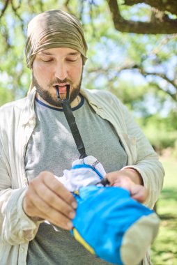 Genç İspanyol bir adam seyahat hamağını kemer ve karabinalarıyla asmak için çıkarıyor. Kavram: açık havada eğlenmek.