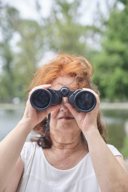 Üst düzey İspanyol kadın dürbün kullanıyor, fotoğrafta kameraya bakıyor. Kavram: Doğayla temasta aktif bir yaşam tarzı sürdürmenin refahı.