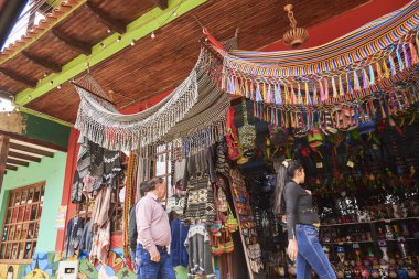 Raquira, Boyaca, Kolombiya; 29 Kasım 2022: Hediyelik eşya ve diğer el işi ürünleri: çantalar, kazaklar, hamaklar, seramik eşyalar, vb. İnsanlar ürünlere bakıyor, manzara çok renkli..