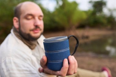 Adam kameraya doğru sabahın erken saatlerinde taze demlenmiş bir fincan kahve sunar. Onun ifadesi sakinlik, sakinlik ve esenlik. El Palmar Ulusal Parkı, Entre Rios, Arjantin.