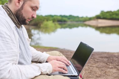 Bir derenin kenarında dizüstü bilgisayarı üzerinde çalışan İspanyol bir adam. Konsept: dijital göçebe seyahat ederken uzaktan çalışıyor, özgürlüğün tadını çıkarıyor.