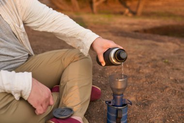 Kahve filtreleme işlemi. İspanyol adam sabahın erken saatlerinde Arjantin 'in Entre Rios kentindeki El Palmar Ulusal Parkı' nda bir derenin kenarında kahvaltıda sıcak su dolduruyor..