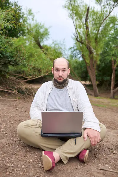 Erkek gezgin dışarıda oturuyor, doğada, dizüstü bilgisayarıyla çalışıyor. Konsept: dijital göçebe seyahat ederken uzaktan çalışıyor, özgürlüğün tadını çıkarıyor.