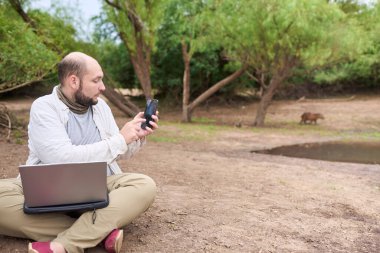 Dizüstü bilgisayarı üzerinde çalışan bir gezgin akıllı telefonuyla geçen bir kapibaranın fotoğrafını çekmek için ara verir. El Palmar Ulusal Parkı, Entre Rios, Arjantin.