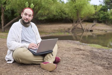 Noel geyiği boynuzu takan genç bir İspanyol adam dışarıda otururken dizüstü bilgisayar kullanıyor. Doğayla iç içe..