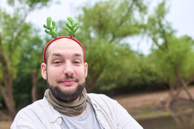 Komik bir Noel geyiği boynuzu takan genç bir İspanyol adam kameraya gülüyor, doğal bir ortamda..