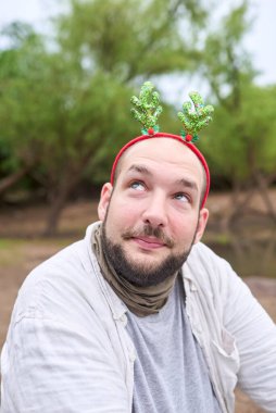 Komik bir Noel geyiği boynuzu takan genç İspanyol bir adam komik bir ifadeyle yukarı bakıyor. O dışarıda, doğada..