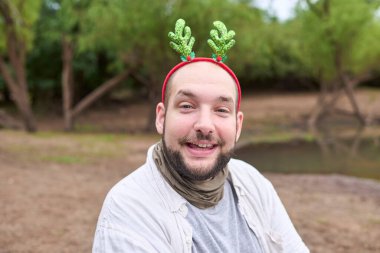 Noel geyiği boynuzu takan genç bir İspanyol adam kameraya gülümsüyor, doğal bir şekilde..