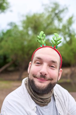 Komik bir Noel geyiği boynuzu takan genç bir İspanyol adam kameraya gülüyor, doğal bir ortamda..