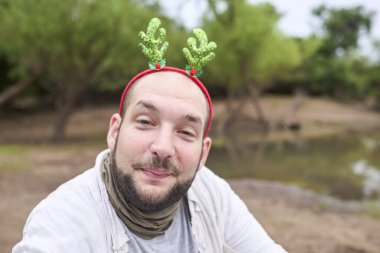 Komik bir Noel geyiği boynuzu takan genç bir İspanyol adam kameraya gülüyor, doğal bir ortamda..