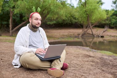 Noel geyiği boynuzu takan genç bir İspanyol adam dışarıda otururken dizüstü bilgisayar kullanıyor. Doğayla iç içe..