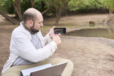 Dizüstü bilgisayarı üzerinde çalışan bir gezgin akıllı telefonuyla geçen bir Capybara 'nın videosunu kaydetmek için ara veriyor. El Palmar Ulusal Parkı, Entre Rios, Arjantin.