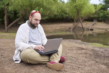 Noel geyiği boynuzu takan genç bir İspanyol adam dışarıda otururken dizüstü bilgisayar kullanıyor. Doğayla iç içe..