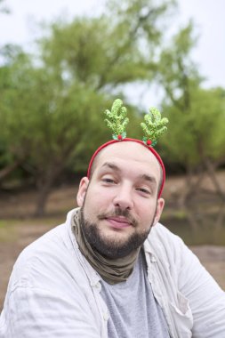 Komik bir Noel geyiği boynuzu takan genç bir İspanyol adam kameraya gülümsedi, doğal bir ortamda..