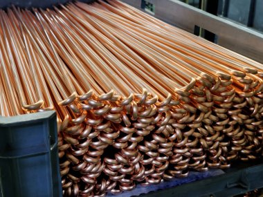 Endüstriyel bir depodaki düzgün istiflenmiş bakır boruların parlak yüzeyleri ve kıvrımlı uçlarını gösteren yakın çekim görüntüsü. İnşaat ve tesisat projeleri için ideal..