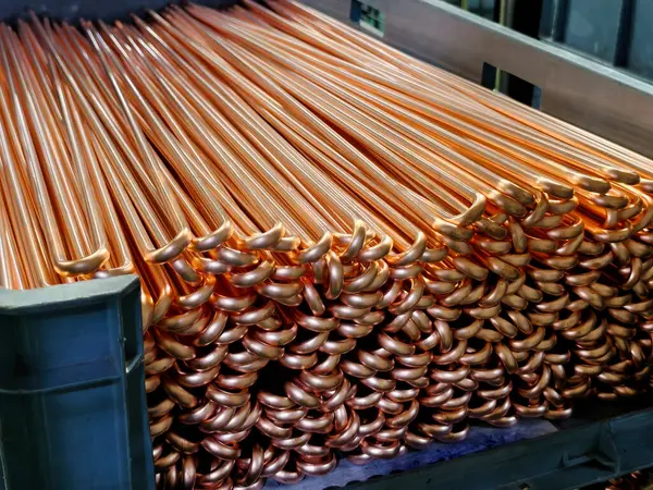 Endüstriyel bir depodaki düzgün istiflenmiş bakır boruların parlak yüzeyleri ve kıvrımlı uçlarını gösteren yakın çekim görüntüsü. İnşaat ve tesisat projeleri için ideal..