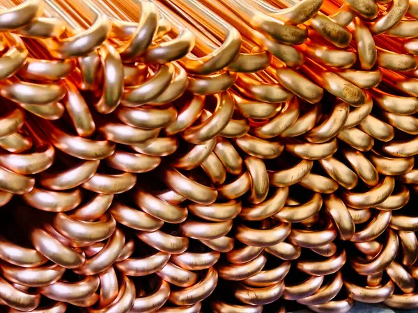 Endüstriyel bir ortamda birbirine kenetlenmiş bakır boruları gösteren detaylı bir yakın çekim görüntüsü. Parlak dokusu ve eşsiz şekilleri işçiliği ve malzeme tasarımını vurguluyor..