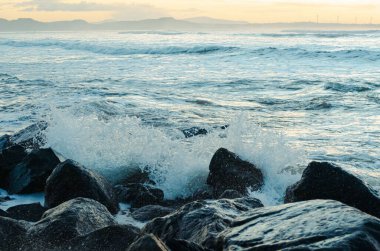 Deniz suyu kayalara çarpar. Deniz dalgaları kıyıdaki kayalara vuruyor. Sonsuz sayıda sıçrama, su damlası ve beyaz köpük dağılmış..