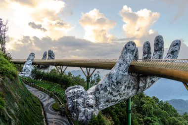 Vietnam 'daki Altın Köprü, iki dev taş el tarafından destekleniyor, yemyeşil yemyeşil bir zemin üzerinde bulutlu bir gökyüzü ile uzanıyor. Doğa ve sanatın çarpıcı bir karışımı..