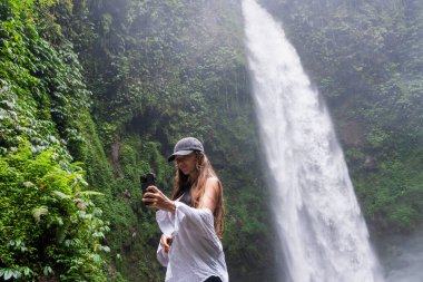 Tarz sahibi genç bir kadın nefes kesici bir tropikal şelalede akıllı telefonuyla macerasını yakalıyor..